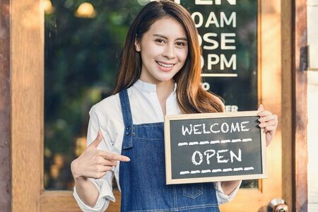 Asian Small business owner hands holding and showing the chalkboard with Welcome Open sign in front of coffee shop, startup with cafe store, installing open and close label conceptの写真素材