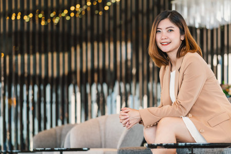 Portrait Asian businesswoman wearing formal suit sitting on the sofa in modern lobby, office or coworking space, coffee break leisure, fashion and lifestyle after working time,business people conceptの写真素材