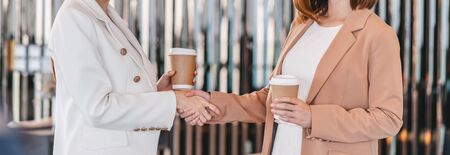 Banner, web page or cover template of Two asian businesswomen holding coffee paper cup and hand shaking when success partner business agreement together, small business with deal completed conceptの写真素材