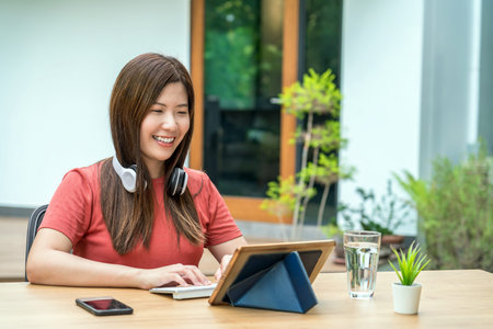 Asian business woman using technology tablet with keyboard and headphone for working from home in...