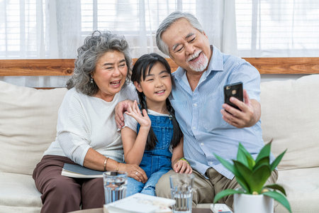 Asian couple Grandparent taking selfie with Granddaughter with happy feeling by mobile phone in house, Long live and Elderly society, Warm family and happiness, leisure and lifestyle conceptの写真素材