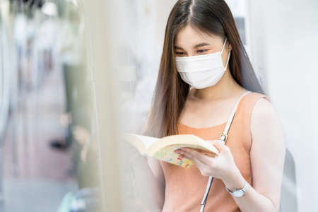 Young Asian woman passenger wearing surgical mask and listening music via smart mobile phone in subway train when traveling in big city at Covid19 outbreak, Infection and Pandemic conceptの写真素材