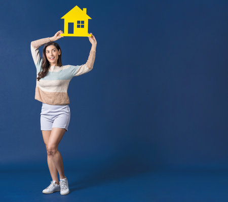 Happy young Asian woman holding and shooting photo with vintage camera on blue color background, carry backpacker and baggage, holiday and travel conceptの写真素材