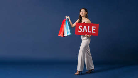 Happy young Asian woman sitting and holding surfskate or skateboard on blue color background, exercise and sport, trendy and extream sports conceptの写真素材