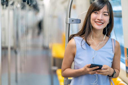 Young Asian woman passenger listening music via smart mobile phone in subway train when traveling in big city,japanese,chinese,Korean lifestyle and daily life, commuter and transportation conceptの写真素材