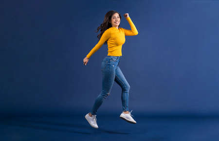 Happy young Asian woman showing credit card and using mobile phone for online shopping on blue color background, cashless payment, black friday and consumerism concept, carrying shopping bagsの写真素材