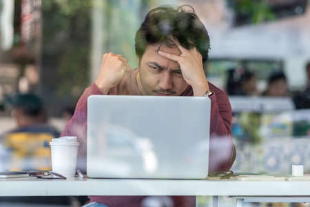 Portrait of asian businessman in casual suit using technology laptop for working in serious and exhausted action at the desk beside the glass in modern office,Business and lifestyle conceptの写真素材