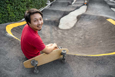 Asian man sitting with surfskate or skate board in pumptrack skate Park when sunrise time over photo blur of pumptrack curve, extream sport, healthy and exercise, fashion in covid19 conceptの写真素材