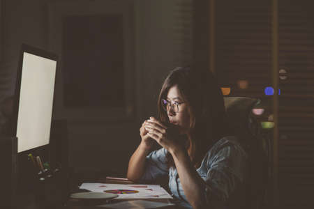 Portrait of Asian Businesswoman sitting and working hard on the table with front of computer desktop in workplace at late with serious action, Work hard and too late conceptの写真素材