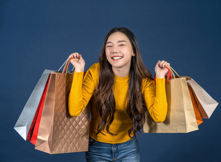 Happy young Asian smiling young woman Carrying a shopping coloful bag on classic blue color...
