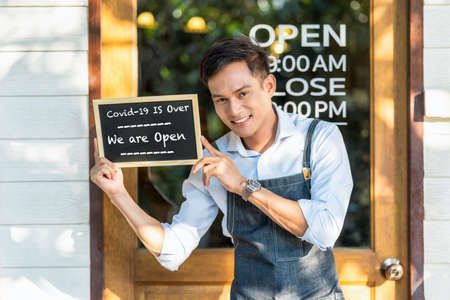 Asian partner Small business owner hands holding and showing the chalkboard with wording Covid-19 is over and we are open sign in front of coffee shop,new normal after Covid gone, coronavirusの写真素材