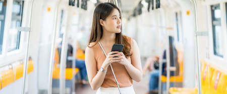 Young Asian woman passenger using smart mobile phone and looking to outside of subway train when traveling in big city, commuter and transportation conceptの写真素材