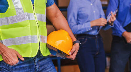 Closeup Indian Worker man hand holding safety helmet over White Caucasian Manager of warehouse worker with Asian assistant manager woman and in local factory, Partner and colleague working togetherの写真素材