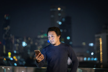 Asian creative freelancer using smart mobile phone with smile action in the financial district area at bangkok river side, Thailand, technology with career conceptの写真素材