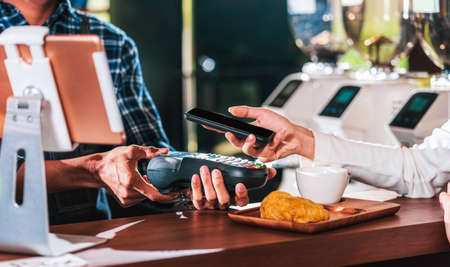 Closeup Asian customer man hand paying money via contactless channel by mobile banking application to Small business owner at table in cafe shop, Small business owner and startup in coffee shopの写真素材