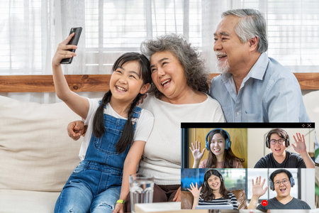 Asian Granddaughter with couple Grandparent taking video call conference to Business people saying hello with teamwork colleague by mobile phone in house, online meeting, Social distancing conceptの写真素材