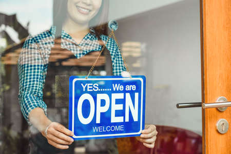 Closeup hand of Asian young woman setting open sign at the shop glasses for welcome the customer in to the coffee shop, small business owner and startup, installing open and close label conceptの写真素材