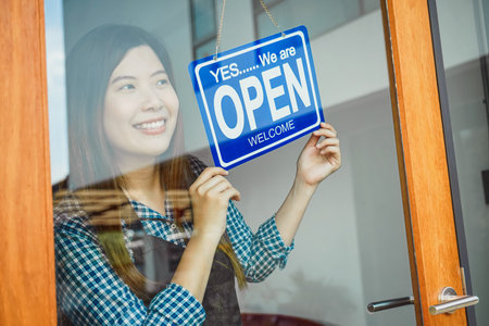 Closeup hand of Asian young woman setting open sign at the shop glasses for welcome the customer in...