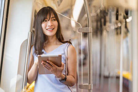Young Asian woman passenger using social network via technology tablet in subway train when traveling in big city,japanese,chinese,Korean lifestyle and daily life, commuter and transportation conceptの写真素材