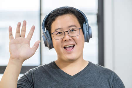 Asian business man waving hand for say hello when making video call to friend with social distancing, smiling female taking video blog recording vlog,  pandemic, headphone and online meetingの写真素材