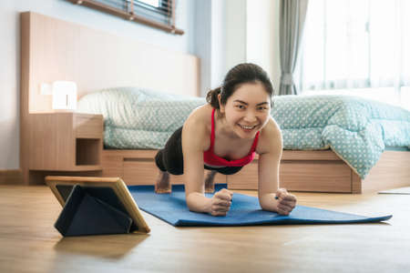 Asian woman practicing yoga from home with laptop when outbreak and lockdown, healthy or Meditation...