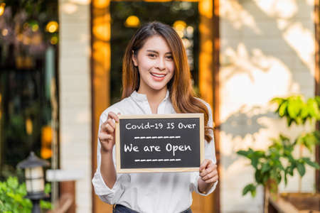 Asian partner Small business owner hands holding and showing the chalkboard with wording Covid-19 is over and we are open sign in front of coffee shop,new normal after Covid gone, coronavirusの写真素材