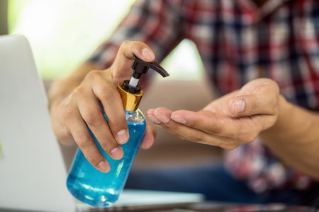 Closeup Asian man using hand sanitizer by pumping alcohol gel and washing before start to work with laptop in work from home period,coronavirus or covid19 outbreak,social distancing and responsibilityの写真素材