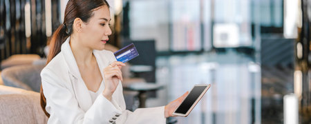 Banner, web page or cover template of Portrait Asian woman using credit card with technology tablet for online shopping in lobby or working space, technology money wallet and online payment conceptの写真素材
