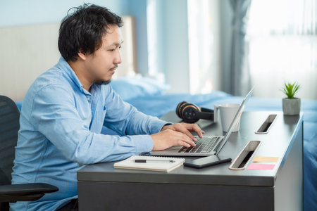 Asian business man using technology laptop and working from home in indoor bedroom of house by video...