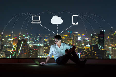 Asian businessman sitting and using the laptop with smart mobile phone for operate various icon of...