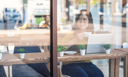 Asian businesswoman drinking and working from home with technology laptop computer in happiness...