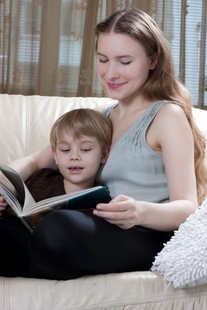 beautiful young mother with her little son reading the book on the sofaの写真素材