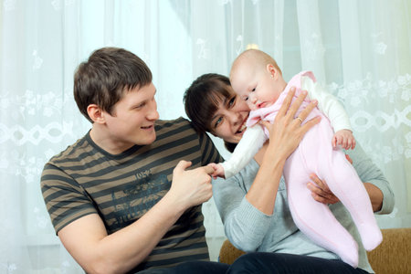 happy family home: father, mother and baby sitting against the window