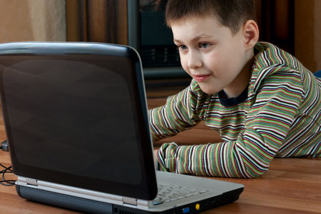 little boy lying down on the floor in the living room and playing computer game on laptop