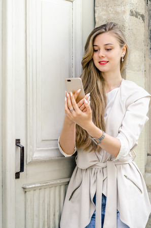 Portrait of a smiling bussines casual woman holding smartphone with long hair in cafe city street sunny day backgroundの写真素材