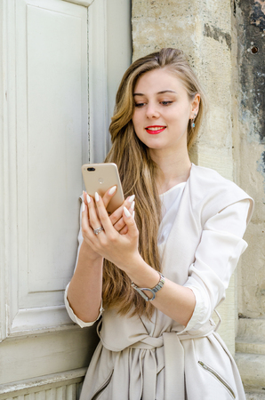 Portrait of a smiling bussines casual woman holding smartphone with long hair in cafe city street sunny day backgroundのeditorial素材