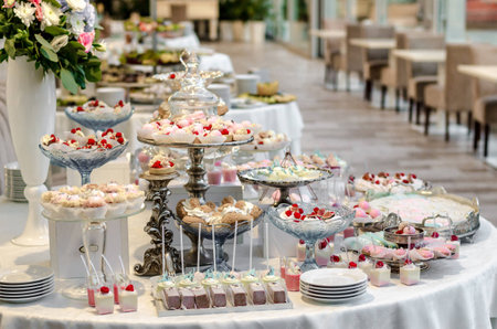 Delicious wedding reception candy bar dessert table full with cakes and sweets and a flower vase with hydrangeas on the background of an exquisite restaurant.の写真素材