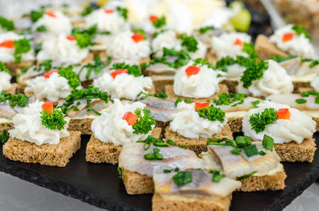 Slices of rye bread wheat bread with herring pieces sprinkled with green onion on a black granite plate.の写真素材