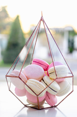 Macarons in a metallic glass vase on a table on the background of a magnificent wedding room. Sweet macarons. Top view with copy space. Party sweets. Happy luxury birthday and wedding concept.の写真素材