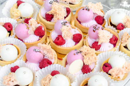 Candy Bar. Sweet round candy in pink and white glaze with raspberries on tartlets. Happy luxury birthday and wedding concept. Party sweets.の写真素材