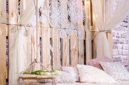 Bedroom loft design with bed soft pillows canopy swing with white tulips dream catcher with feathers and pearls hanging on a wooden backgroundの写真素材