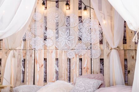 Bedroom loft design with bed soft pillows canopy swing with white tulips dream catcher with feathers and pearls hanging on a wooden backgroundの写真素材
