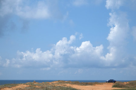 Small car stands at a corner of landscape with the image of clouds under the sea beachの写真素材