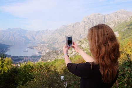 Girl tourist photographs a landscape with sea and mountains in Kotor, Montenegro