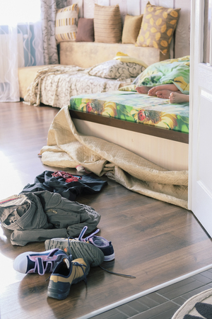 Clothes scattered on a floor of a bedroom and a pair of legs, looking ouy from under a blanketの写真素材