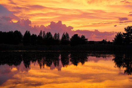 Beautiful sunset on the lake in the summer. Colorful sky with clouds reflected in the water.