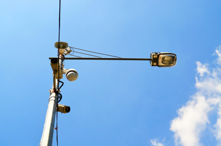 Loudspeaker and CCTV camera on lamp post against blue skyの写真素材