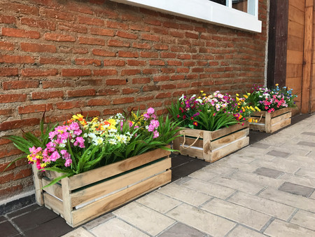 Colorful artificial flower in wooden box decorated in front of brick wallの写真素材