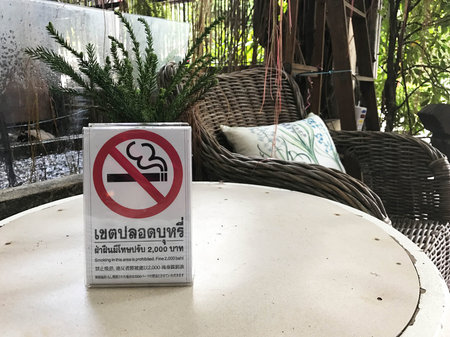No smoking sign at on table at rest area in the garden. Thai word stated "No smoking, fine 2,000 Bath"の写真素材