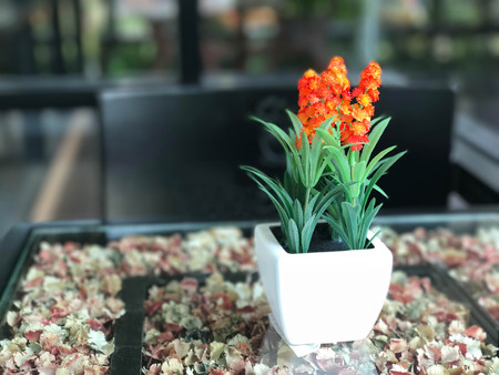 Orange artificial flower with green leaf in white flower pot on table in coffee shop, selective focusの写真素材